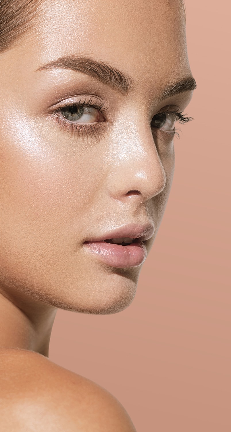 Smiling woman with soft makeup against brown backdrop.